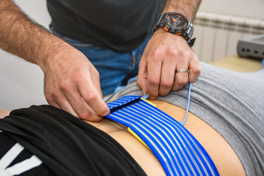 Man's hands adjusting electrostimulation pads on a woman's back. Back pain, therapy.
