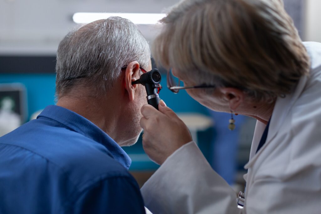 Woman doctor holding otoscope to do ear consultation for old man at medical appointment
